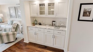 A kitchen with white cabinetry, a marble countertop, and a dining area with a striped chair. - Paradise Found Beachfront Litchfield By the Sea (Pawleys Island)