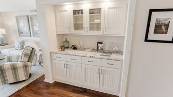 A kitchen with white cabinetry, a marble countertop, and a dining area with a striped chair.