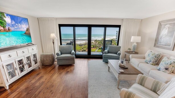 A spacious living room with a large TV, two armchairs, a sofa, and a balcony with ocean views. - Paradise Found Beachfront Litchfield By the Sea (Pawleys Island)