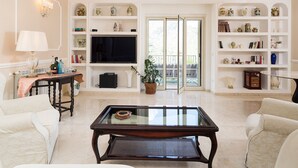 A living room with a glass-top coffee table, white sofas, a television, and decorative shelves. - Pool villa in Castelmola, Taormina, Sicily (Castelmola)