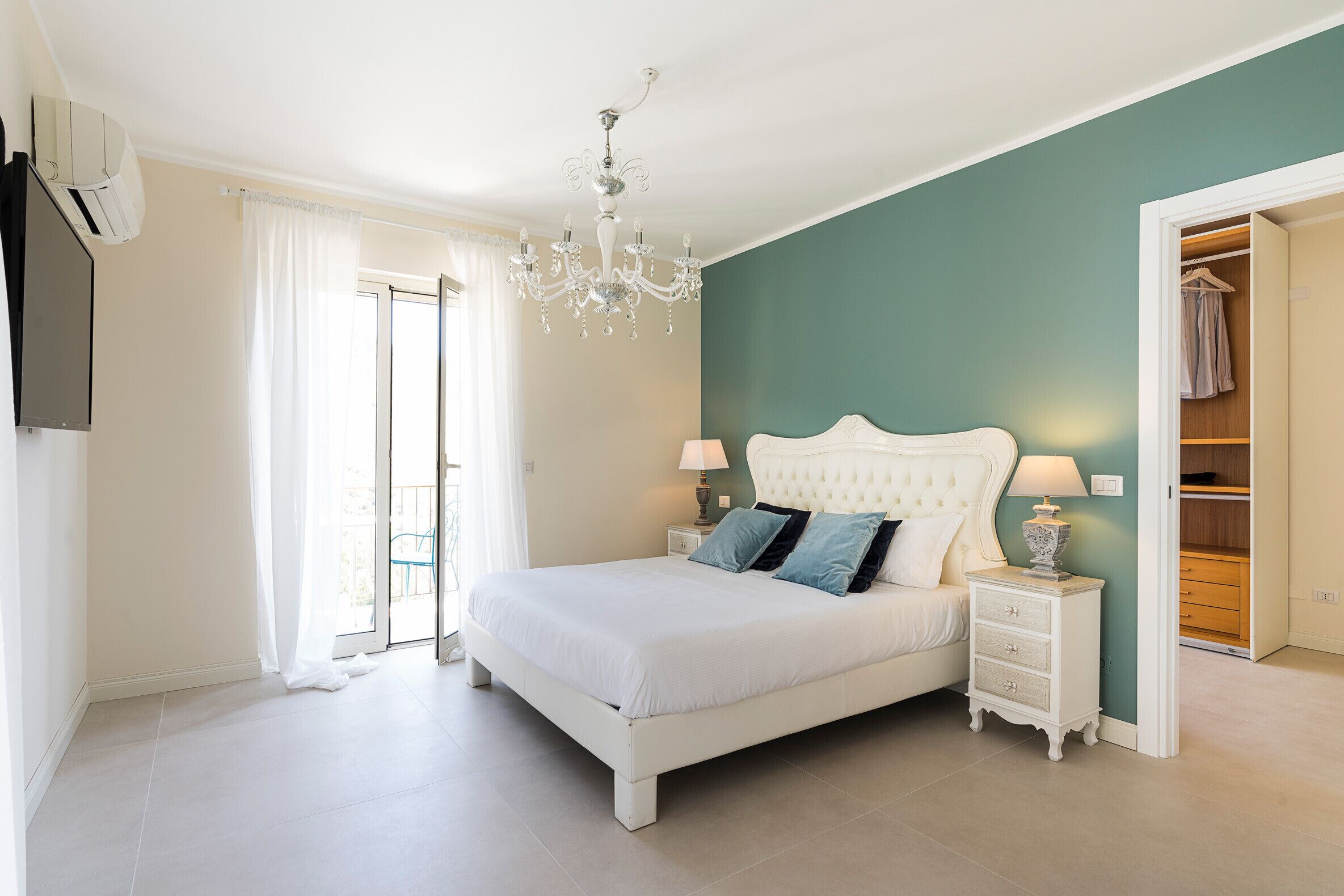 A bedroom with a white bed, a chandelier, a nightstand, and a wardrobe.