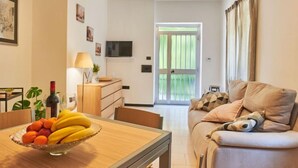 A living room with a sofa, a dining table with fruit, a lamp, and a TV on the wall. - Apartment Dani by Interhome (Colico)
