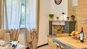 A modern living room with a sofa, a dining table with chairs, a fireplace with a brick surround, and a clock on the wall. - Apartment Dani by Interhome (Colico)
