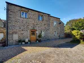 A stone building with a wooden door, multiple windows, and a gravel driveway.