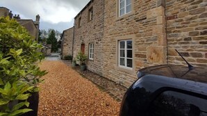 Un bâtiment en pierre avec une allée gravillonnée et une voiture garée.