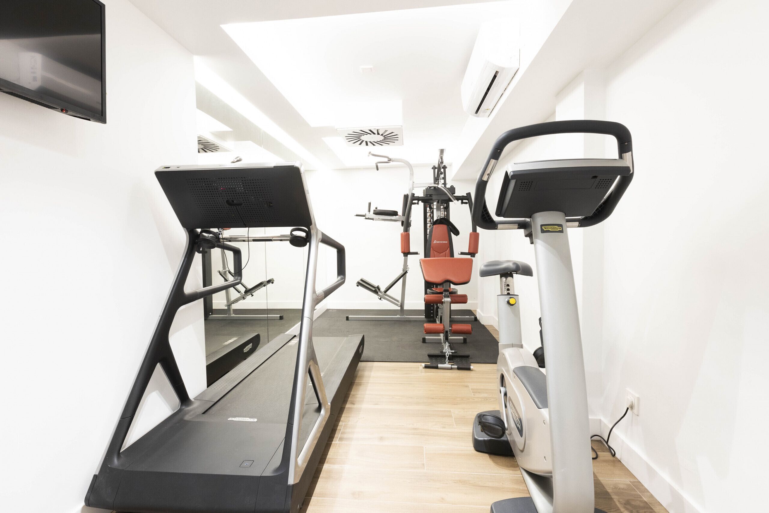Une salle de sport équipée de tapis de course, d’appareils de musculation et d’un écran de télévision.