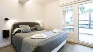 A modern bedroom with a large bed, a nightstand, and a window with a view of palm trees. - Villa Carmen by Basquelidays (Hondarribia)