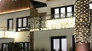 Un immeuble à plusieurs étages doté d’un balcon, de grandes fenêtres et d’un arbre décoré de guirlandes lumineuses.
