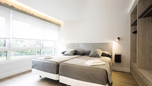 Une chambre moderne avec une grande fenêtre, un lit doté de deux matelas blancs et une armoire en bois.