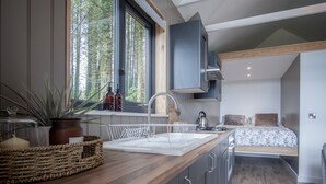 A modern kitchen with a wooden countertop, built-in cabinets, and a window with a view of trees. - Cabin In The Woods - 1 Bed - Kilgetty (Kilgetty)
