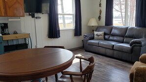Een gezellige woonkamer met een houten eettafel, een leren bank en een koffieapparaat.