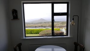 A room with a round table and two chairs, a window with a view of a landscape, and a wall-mounted clock. - Lovely 3-bed House in Connemara, County Galway (Gowla)