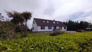 A white house with a tiled roof, surrounded by lush green hedges and a palm tree. - Lovely 3-bed House in Connemara, County Galway (Gowla)