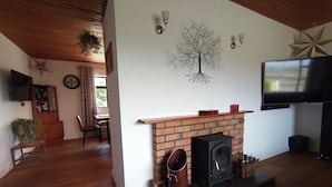 A living room with a brick fireplace, a television mounted on the wall, and a star decoration on the ceiling. - Lovely 3-bed House in Connemara, County Galway (Gowla)