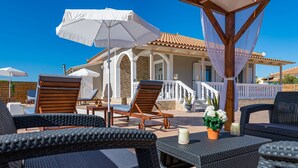 A covered outdoor seating area with wicker furniture and white umbrellas, overlooking a building with a tiled roof and stone walls. - Blossom Villa (Zakynthos)