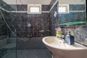 A bathroom with a marble shower, a sink with a soap dispenser, and a small window above the mirror. - Blossom Villa (Zakynthos)