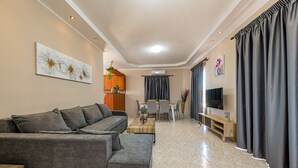 A modern living room with a grey sofa, a wooden coffee table, and a dining area with a table and chairs. - Blossom Villa (Zakynthos)