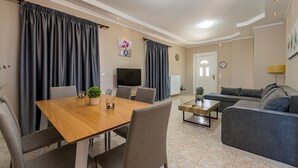 A modern living room with a wooden dining table, grey sofa, and a TV. - Blossom Villa (Zakynthos)