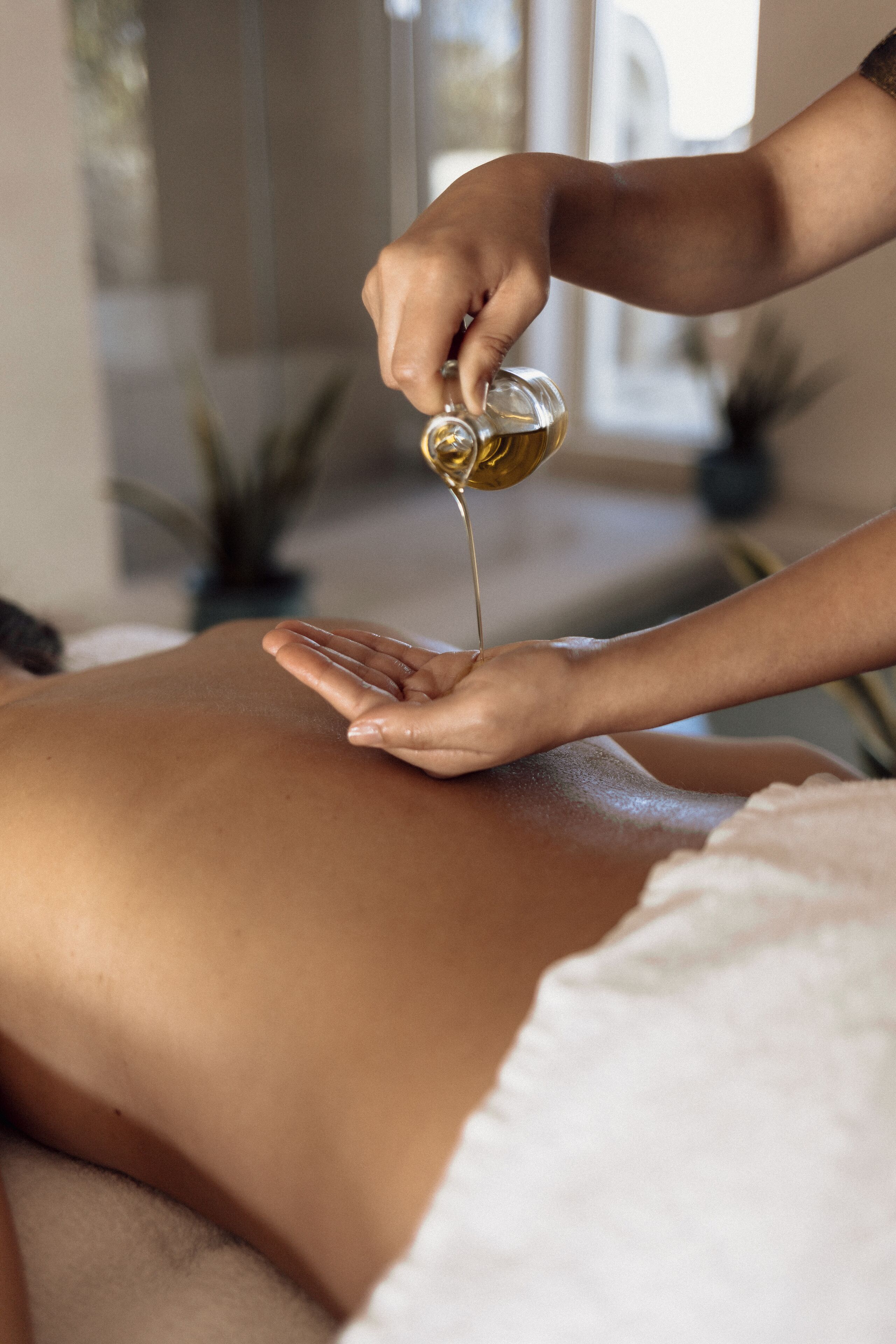 A person receiving a massage with oil being applied to their back.