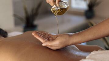 A person receiving a massage with oil being applied to their back.
