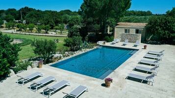 Una piscina con sillones de descanso y un edificio de piedra al fondo.