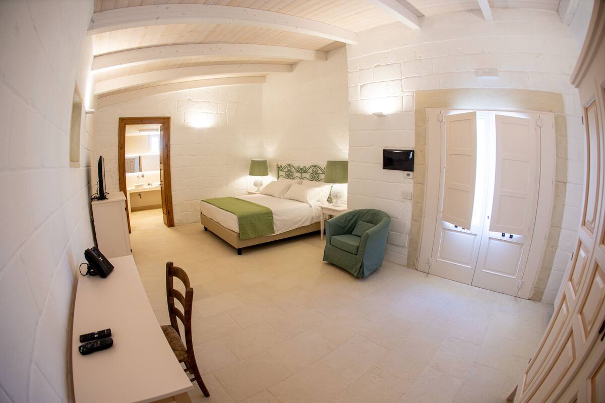 Ein Schlafzimmer mit Bett, Stuhl, Schreibtisch und Fernseher.