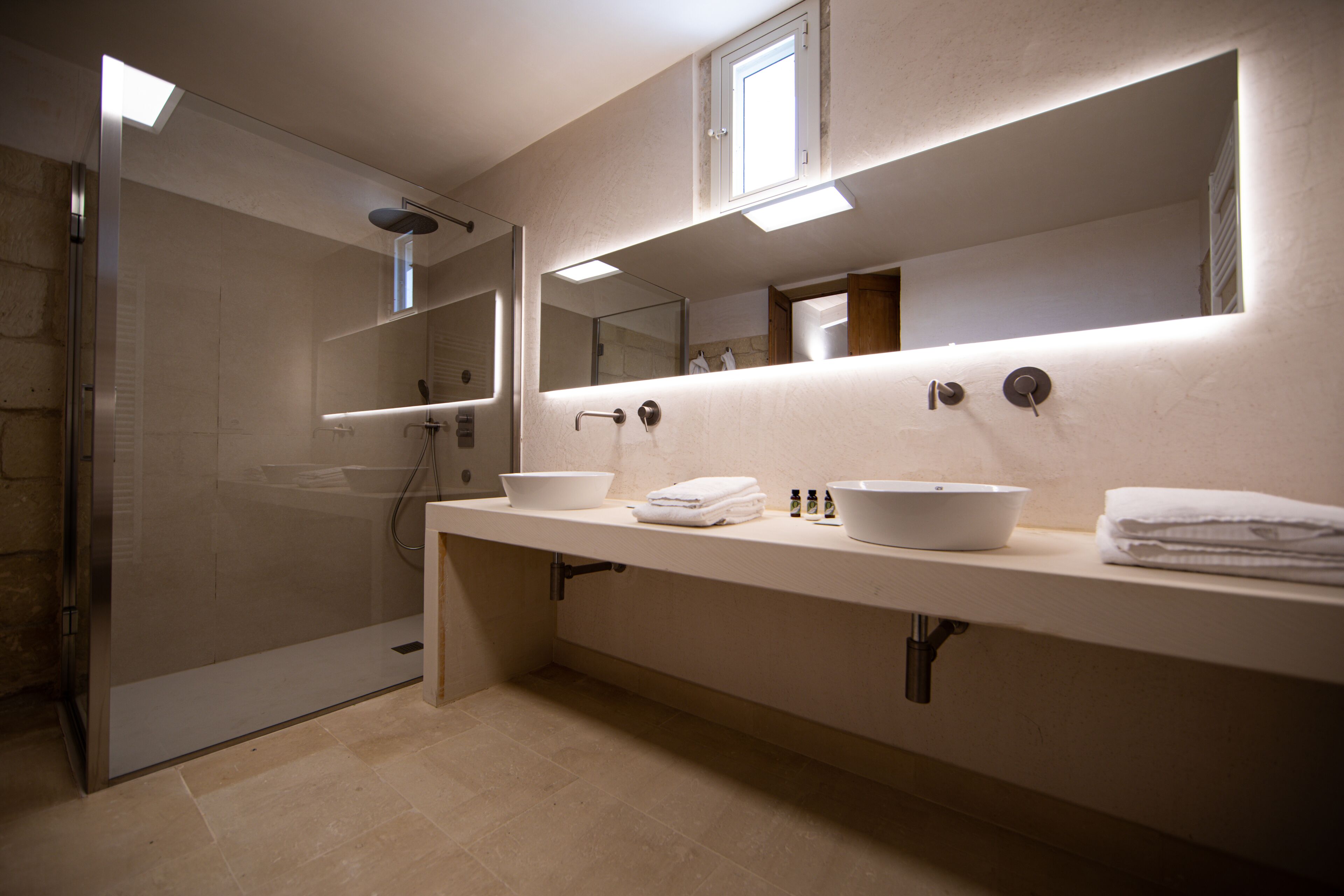 Un baño moderno con ducha de vidrio, un espejo grande sobre el lavabo y una encimera con artículos de aseo.