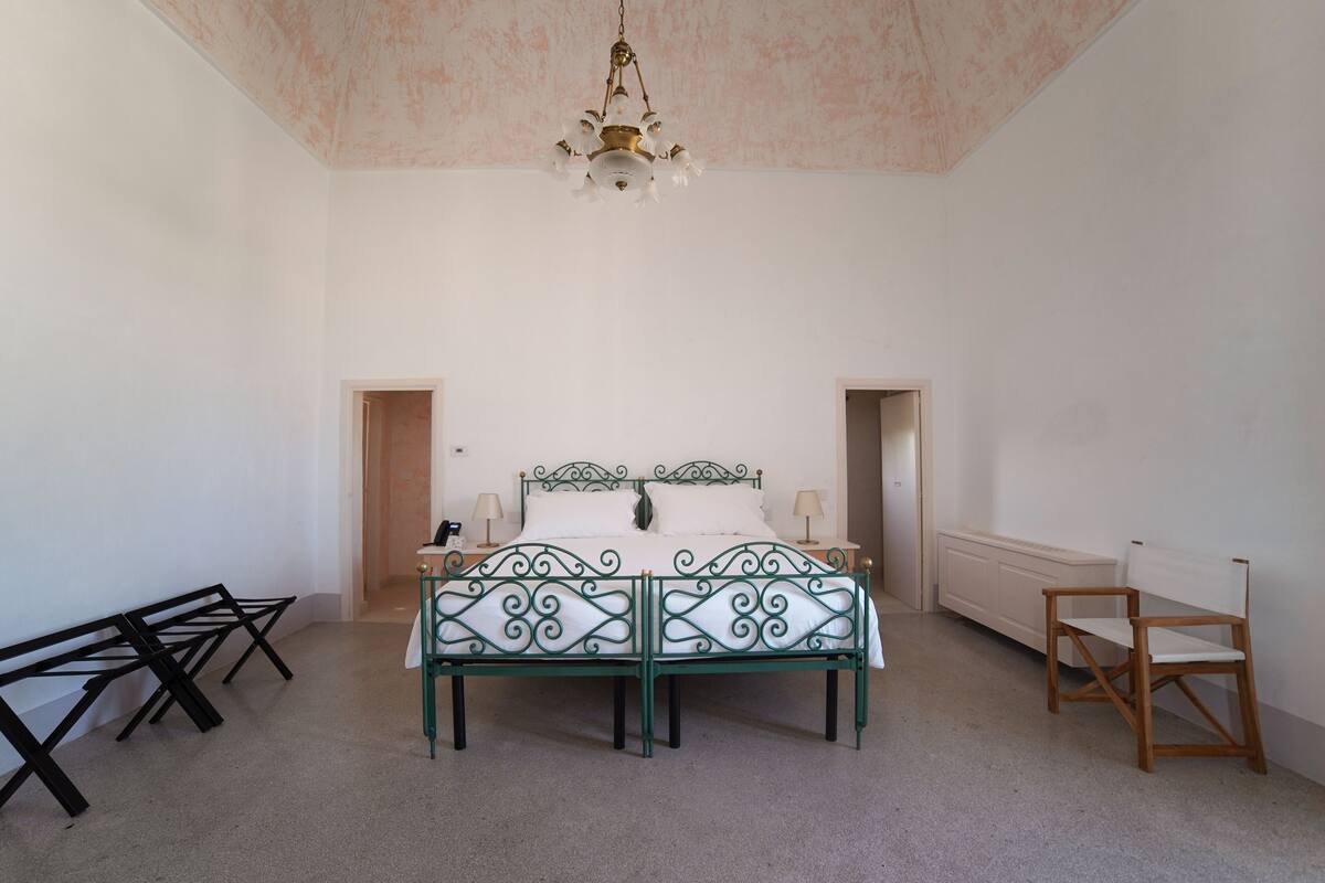 Ein Schlafzimmer mit einem Bett, zwei Nachttischen, einem Sessel und einer Deckenleuchte.