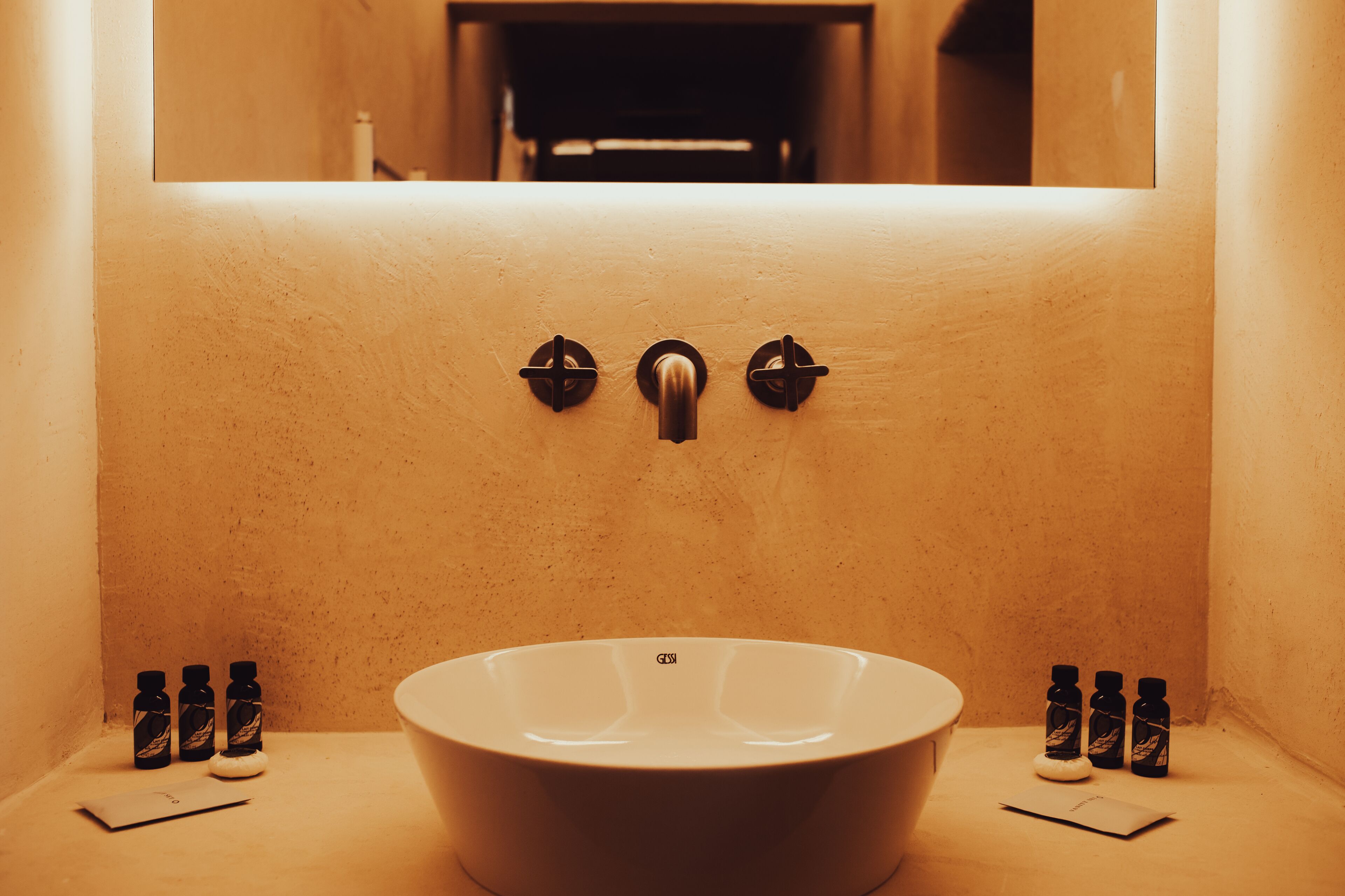 A bathroom with a large sink, three bottles of shampoo, and a mirror above the sink.