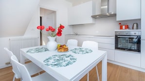 A modern kitchen with white cabinetry, a built-in oven, and a dining table with floral placemats. - GuestHost - The property enjoys a strategic position, just a few steps from the historic center and only 10 minutes by car from the hospital. Its location makes the apartment perfect for any type of trip: nearby, you can find typical bars, ethnic restaur (Udine)