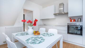 Una cucina moderna con mobili bianchi, forno integrato e tavolo da pranzo con sottopiatti floreali.