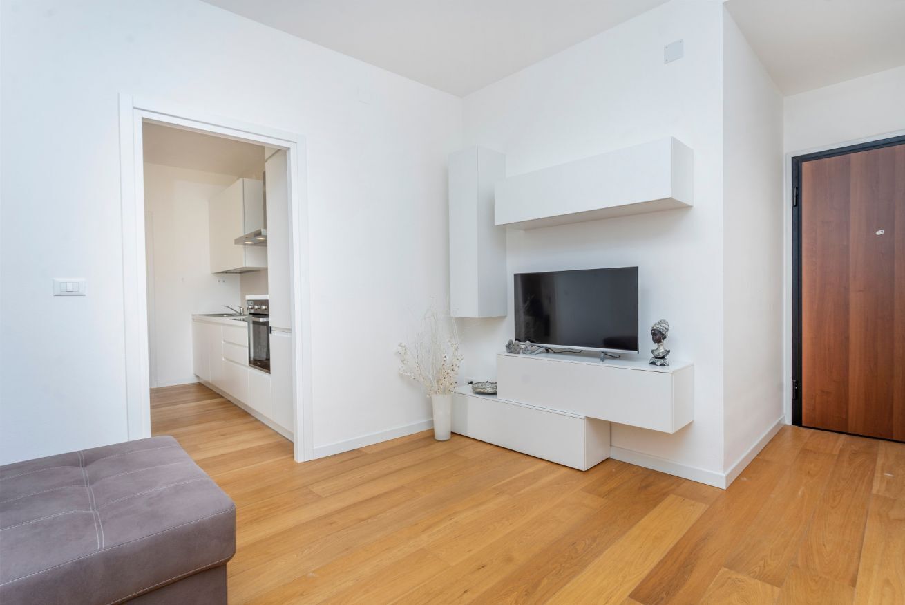 Un soggiorno moderno con una televisione a schermo piatto, un divano grigio e un pavimento in legno.