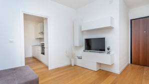 A modern living room with a flat-screen TV, a grey sofa, and a wooden floor. - GuestHost - The property enjoys a strategic position, just a few steps from the historic center and only 10 minutes by car from the hospital. Its location makes the apartment perfect for any type of trip: nearby, you can find typical bars, ethnic restaur (Udine)