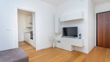Un soggiorno moderno con una televisione a schermo piatto, un divano grigio e un pavimento in legno.