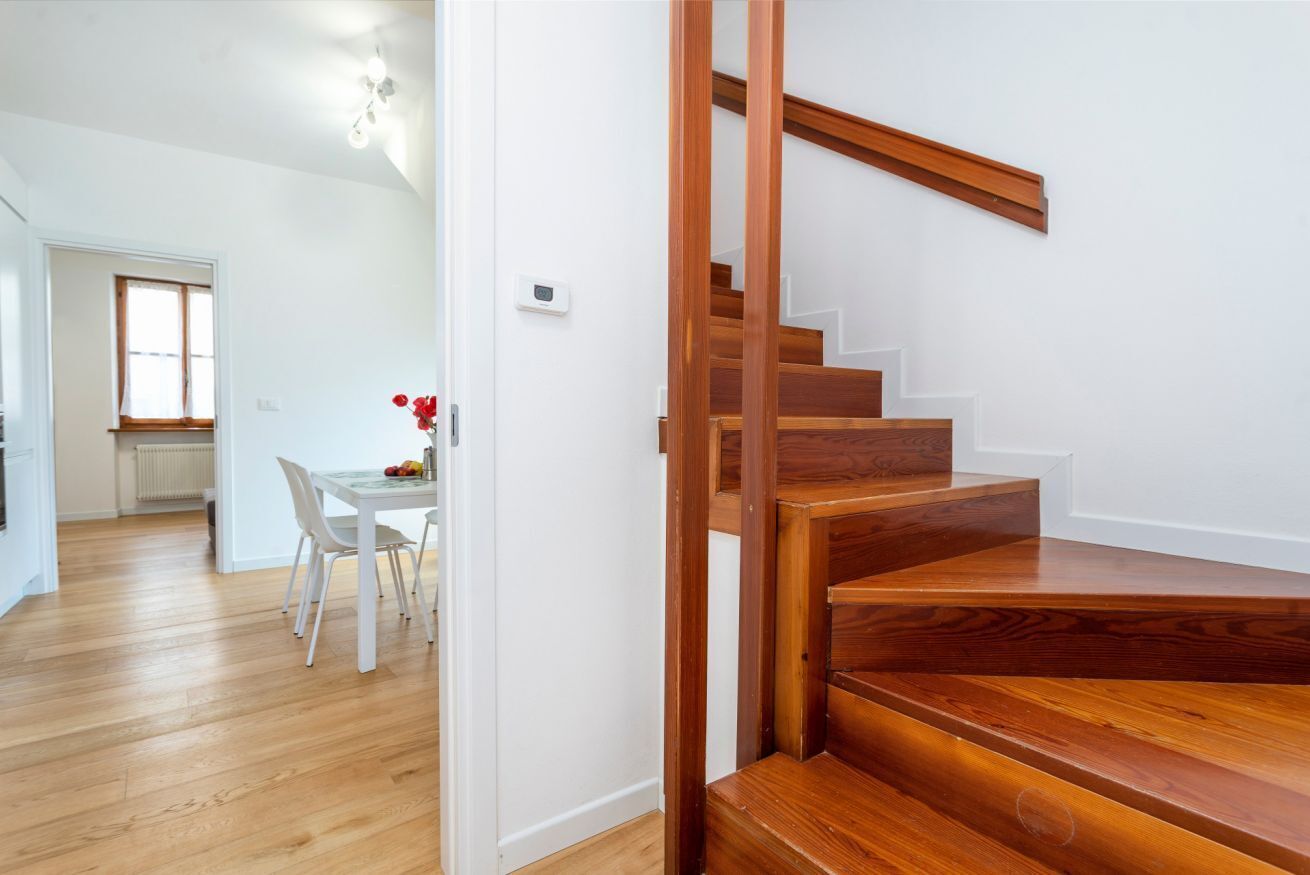Eine Holzt Treppe führt zu einer zweiten Etage, einem Essbereich mit Tisch und Stühlen und einem Fenster mit Tageslicht.