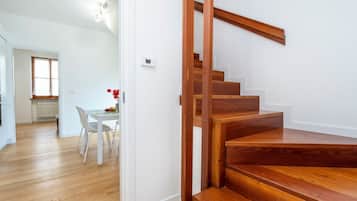 Eine Holzt Treppe führt zu einer zweiten Etage, einem Essbereich mit Tisch und Stühlen und einem Fenster mit Tageslicht.