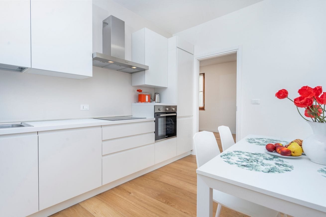 Una cucina moderna con mobili bianchi, un forno in acciaio inossidabile e un'area pranzo con tavolo e sedie bianche.