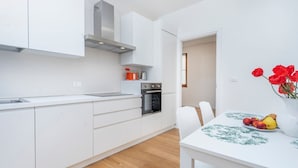 A modern kitchen with white cabinetry, a stainless steel oven, and a dining area with a white table and chairs. - GuestHost - The property enjoys a strategic position, just a few steps from the historic center and only 10 minutes by car from the hospital. Its location makes the apartment perfect for any type of trip: nearby, you can find typical bars, ethnic restaur (Udine)