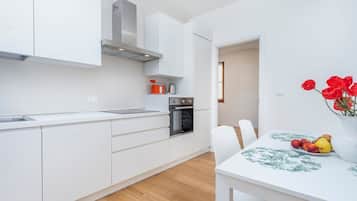 Una cucina moderna con mobili bianchi, un forno in acciaio inossidabile e un'area pranzo con tavolo e sedie bianche.