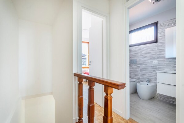 Un interior moderno con una escalera de madera, un baño con bidé y lavamanos, y vista al exterior.