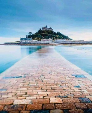 Un sentier pavé mène à un château situé sur une colline, d’où l’on a une vue sur un plan d’eau.