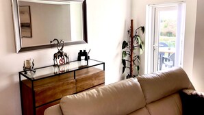 A modern living room with a glass coffee table, a sofa, a wooden cabinet, a large mirror, and a potted plant. - Convenient located. Bright, Spacious , Amazing View Of St Michaels Mount and Sea (Marazion)