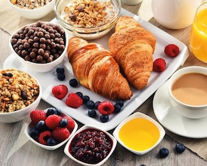 Uma mesa de café da manhã com croissants, frutas vermelhas, granola e uma xícara de café.