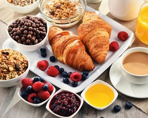 Desayuno con cruasanes, bayas, granola y una taza de café.