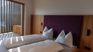 Ein Doppelbett mit weißer Bettwäsche und Kissen, ein Holzkopfschild und Blick durch ein großes Fenster.