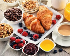 A breakfast setting with croissants, berries, granola, and a cup of coffee.