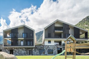 Un bâtiment moderne à deux étages, doté de balcons, d’une façade en pierre et d’une aire de jeux.