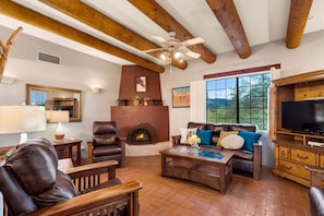 A living room with a fireplace, leather furniture, a television, and a large window. - Cereus Vista- Outstanding Views (Tucson)