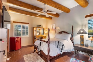 A bedroom with a wooden four-poster bed, a ceiling fan, a red refrigerator, a wooden desk, and a window with shutters. - Cereus Vista- Outstanding Views (Tucson)