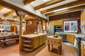 A rustic kitchen with wooden beams, a central island, and a dining area with benches.